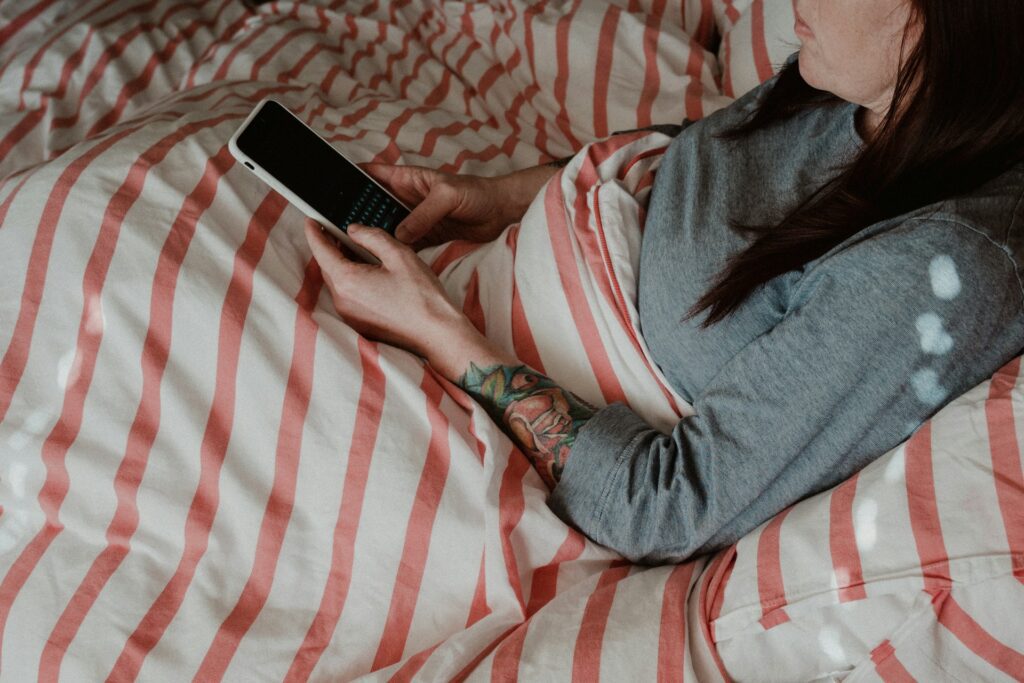 Valokuva naisesta, joka käyttää kännykkää sängyssä.