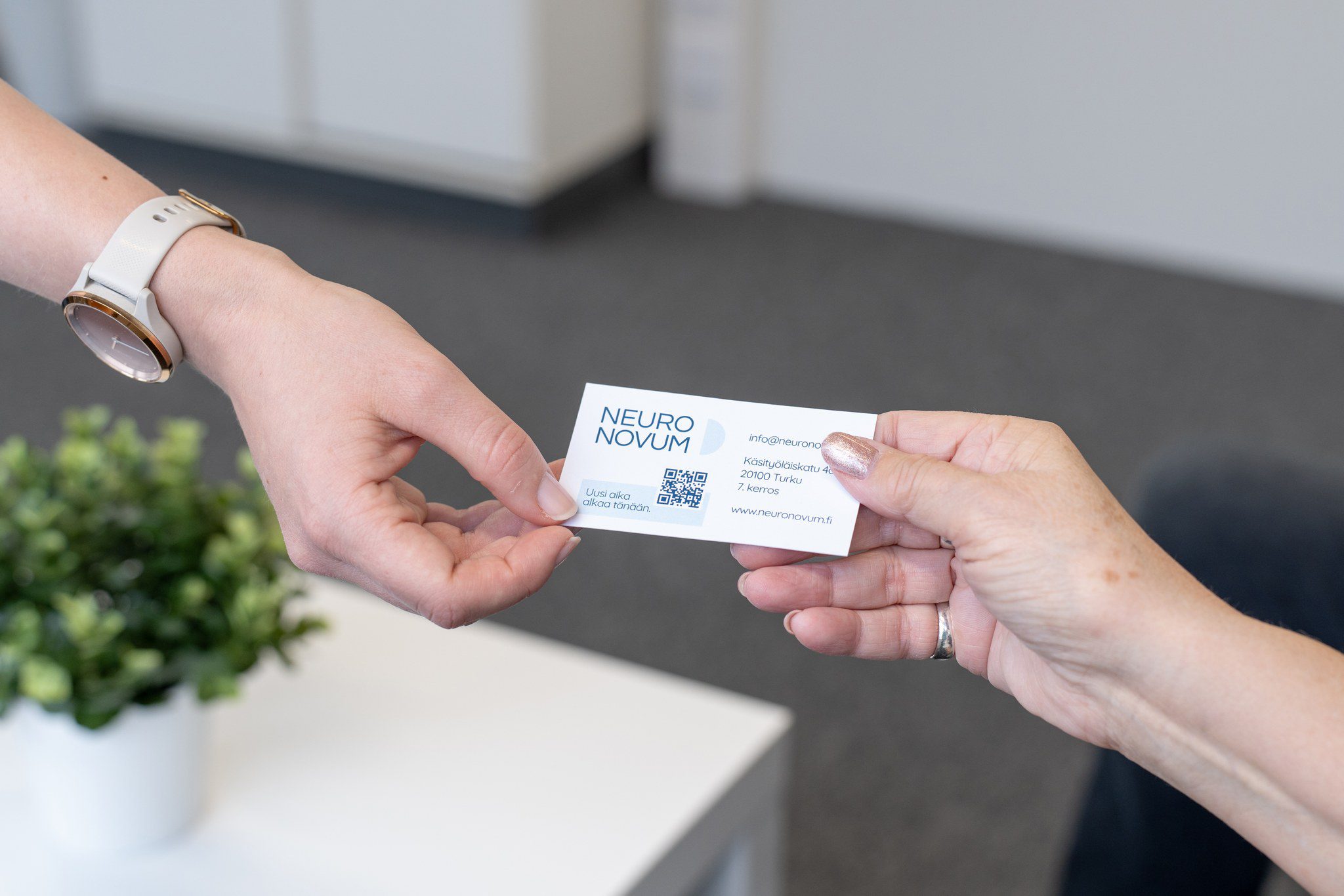 Valokuvassa ojennetaan käyntikorttia, jossa näkyy Neuronovumin yhteystiedot